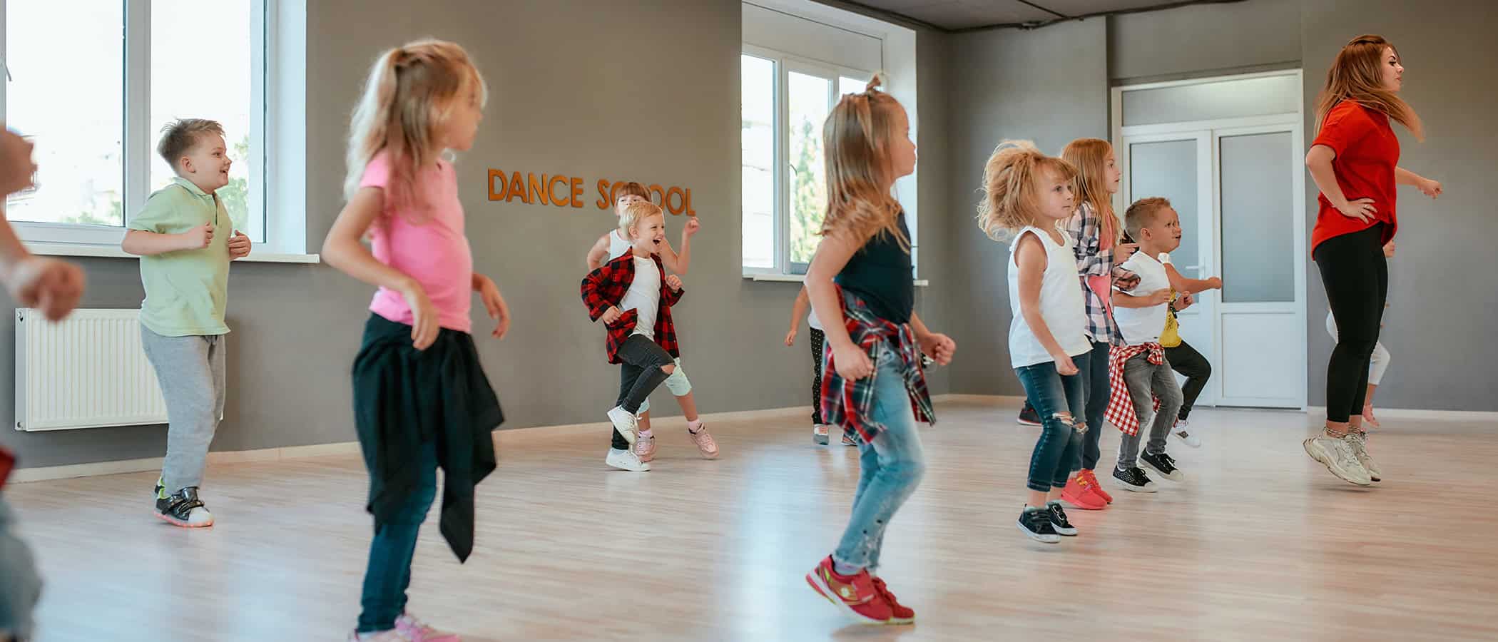 Group of active children dancing in front of the large mirror while having choreography class in the dance studio. Female dance teacher and kids. Contemp dance. Hip hop. Full length